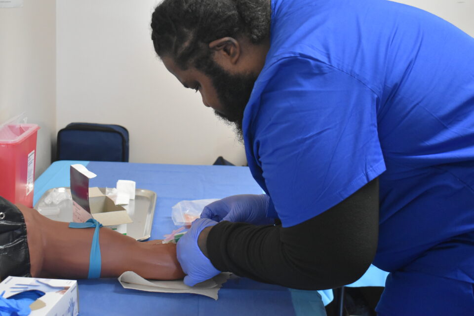 Student administering needle in prosthetic arm